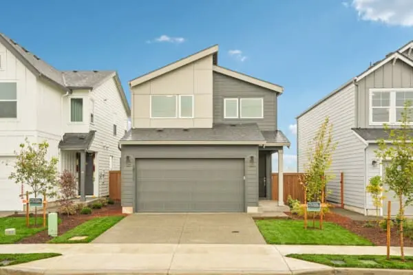 A modern, two-story gray house with a double garage door, neatly landscaped front yard, and a clear blue sky overhead, flanked by two similar houses on either side.