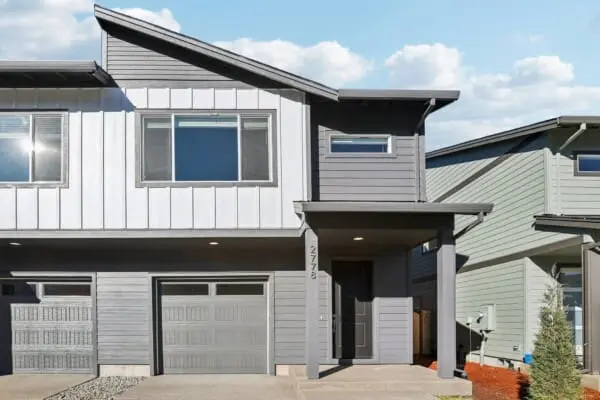 Modern two-story townhouse with gray siding, a single-car garage, large windows, and a covered front entryway, located in Pleasant Valley Villages at 11241 SE Pleasant Valley Parkway under a blue sky with scattered clouds.