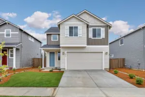 Modern two-story house with gray and white exterior, attached two-car garage, manicured lawn, and neighboring homes on both sides under a blue sky with clouds.