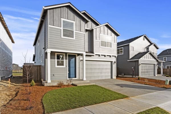 The elegant gray house at 206 S 88th Dr features a striking blue front door and a spacious double garage. A neat lawn with freshly planted shrubs adorns the front yard. Under the clear sky, neighboring homes of Greely 77 add to the picturesque setting on this serene street.