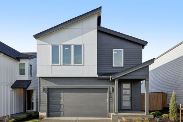 Modern two-story house with a mix of white and dark gray siding, large windows, a double garage with frosted glass panels, and a small front porch, set against a clear blue sky.